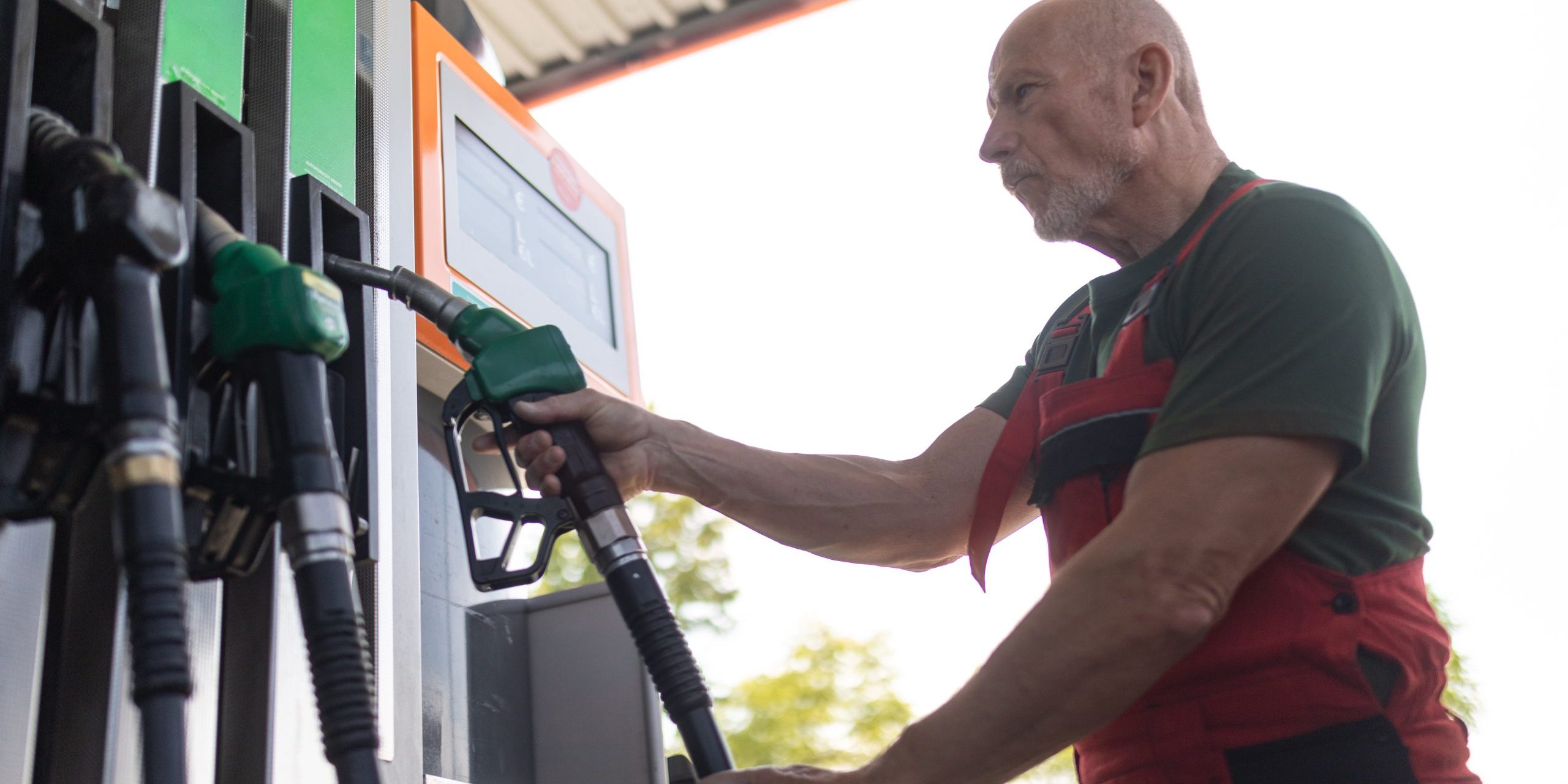 Senior worker standing on gas station and fueling car.