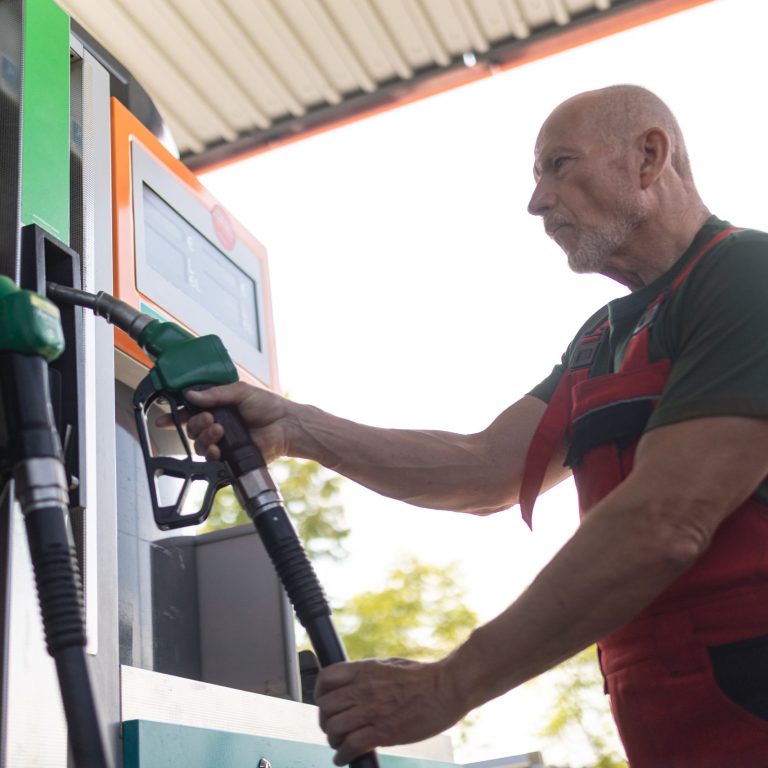 Senior worker standing on gas station and fueling car.
