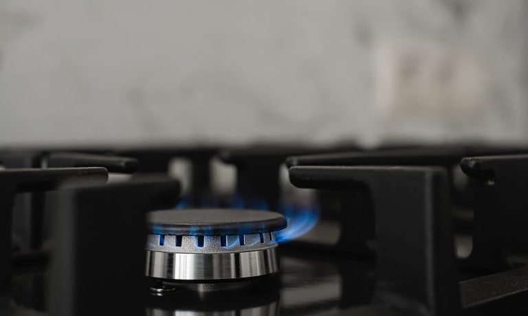 Modern kitchen stove, natural gas burns with a blue flame. Household gas consumption. Close-up, selective focus