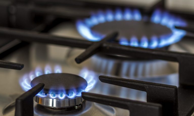 Natural gas burning on kitchen gas stove in the dark. Panel from steel with a gas ring burner on a black background, close-up shooting