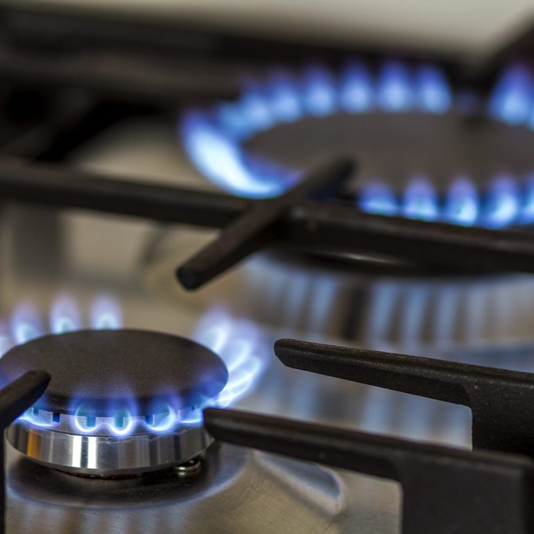 Natural gas burning on kitchen gas stove in the dark. Panel from steel with a gas ring burner on a black background, close-up shooting