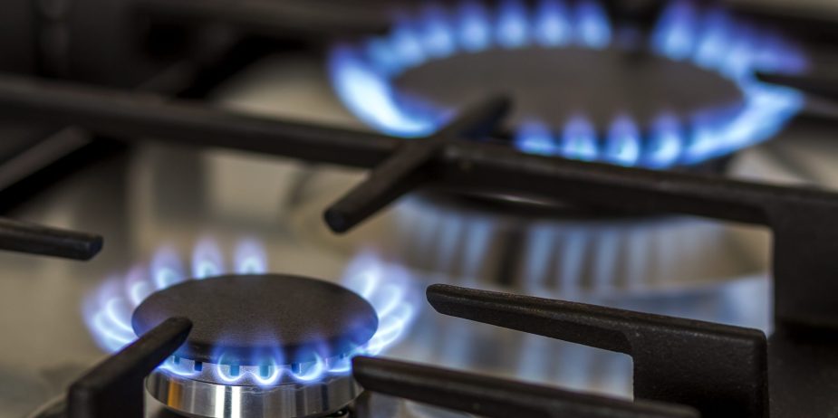 Natural gas burning on kitchen gas stove in the dark. Panel from steel with a gas ring burner on a black background, close-up shooting