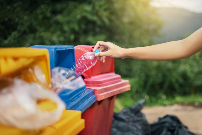 hand holding bottle plastic garbage into trash in park