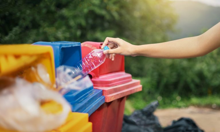 hand holding bottle plastic garbage into trash in park
