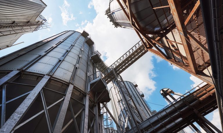 Agricultural Silos. Building Exterior. Storage and drying of grains, wheat, corn, soy, sunflower against the blue sky with white clouds