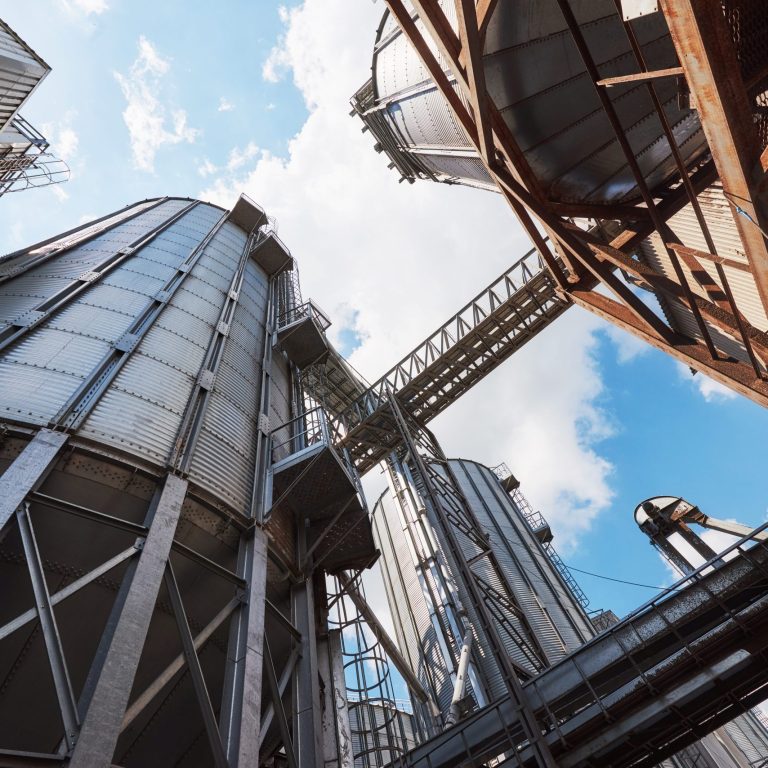 Agricultural Silos. Building Exterior. Storage and drying of grains, wheat, corn, soy, sunflower against the blue sky with white clouds
